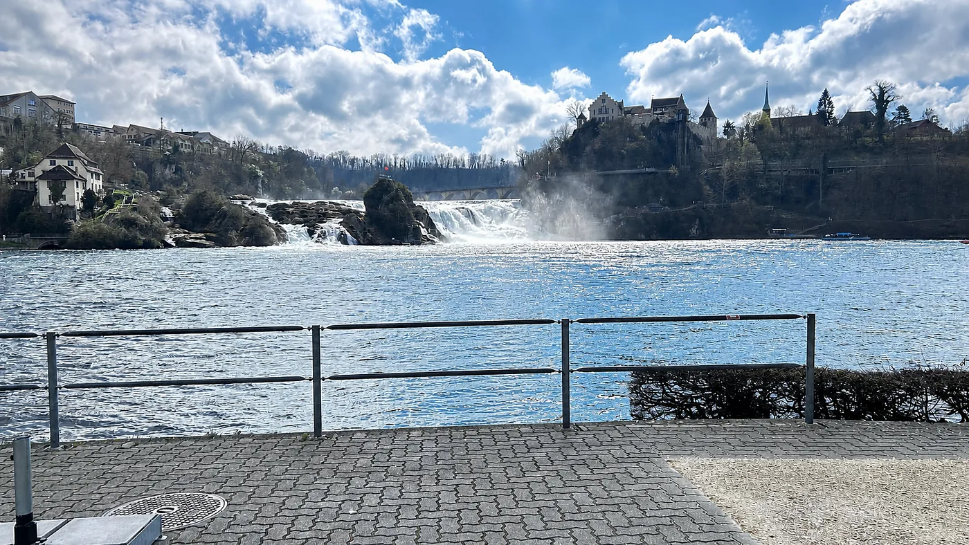 The Rhine Falls, a broad curtain of water with a hilltop castle beyond